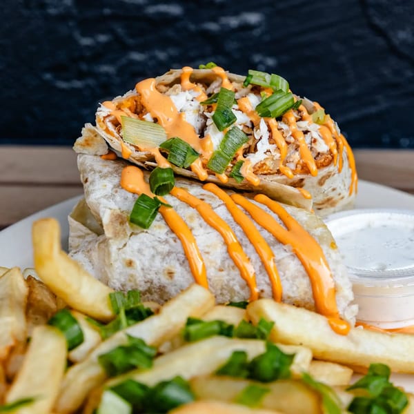 Two burritos drizzled with orange sauce and green onions, served with french fries and a side of dip.