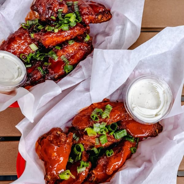 Two baskets of saucy chicken wings topped with green onions and served with ranch dressing.